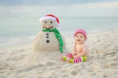 a baby sitting in front of a snowman on the beach