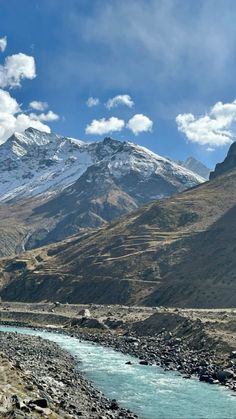 a river running through a valley with snow covered mountains in the backgrouds