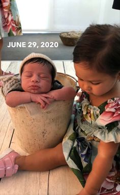 two young children sitting next to each other on a wooden floor and one is holding the baby's head