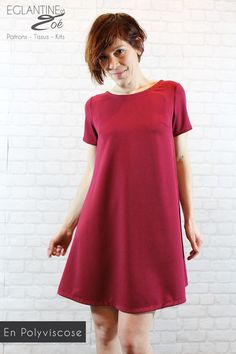 a woman standing in front of a white brick wall wearing a red dress and smiling