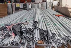 several steel pipes stacked on top of each other in a warehouse area with workers working behind them