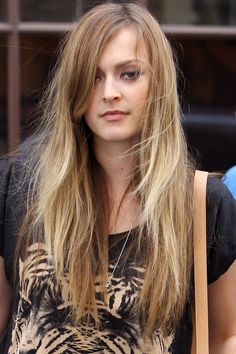 a woman with long blonde hair is looking at the camera while holding a brown bag