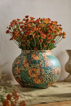 a vase filled with lots of orange flowers on top of a table next to other vases