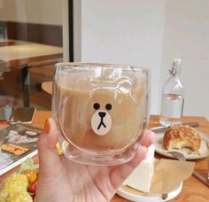 a person holding up a cup with a bear face on the side and some food in front of them