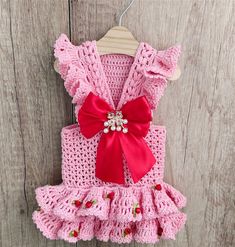 a pink crocheted dress with a red bow