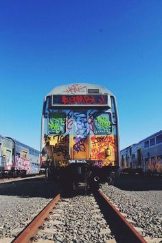 a train covered in graffiti sitting on top of train tracks next to another train car