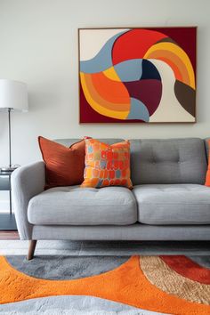 a gray couch with orange and blue pillows on it in front of a large painting