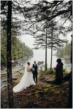 a bride and groom are standing in the woods by the water with their wedding party