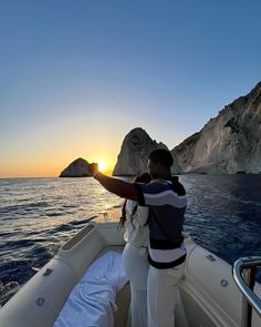 a man on a boat pointing at the sun setting over an island in the ocean