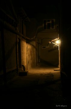 a dark alley way at night with an open door and street lamp on the side