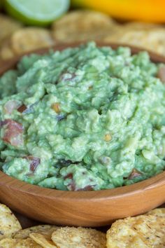 a wooden bowl filled with guacamole surrounded by chips