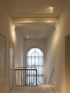 an empty hallway leading to a large arched window and metal handrail with railings