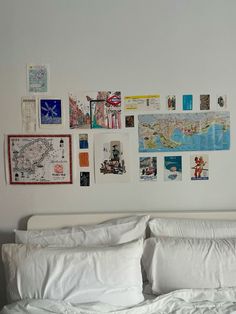 a white bed topped with lots of pillows next to a wall covered in pictures and postcards