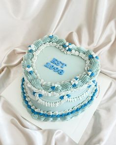 a heart shaped cake on top of a white sheet covered table with blue frosting