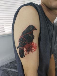 a man with a black bird tattoo on his arm and red string wrapped around it