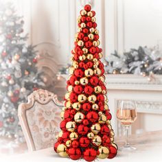 a red and gold christmas tree sitting on top of a table next to a glass of wine