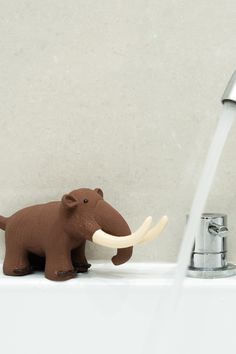 a brown elephant figurine sitting on top of a sink next to a faucet