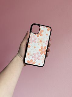 a hand holding an iphone case with flowers painted on the front and back cover, against a pink background