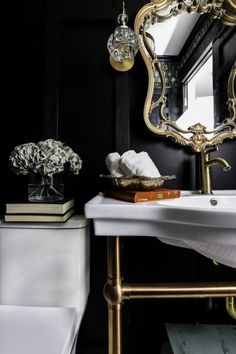 a white toilet sitting next to a bathroom sink under a large mirror and gold faucet