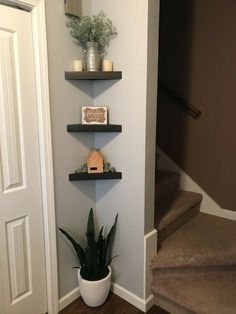 three shelves with plants and candles on them in the corner of a room next to stairs