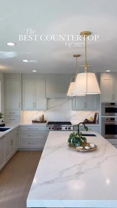 a large white kitchen with marble counter tops and an island in front of the sink