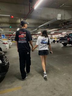 a man and woman holding hands walking through a parking garage with cars parked in the background