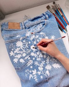 someone is doing something on their jean pants with paintbrushes and pencils next to them