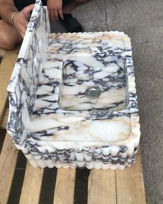 a man kneeling down next to a white and black marbled box on wooden pallets