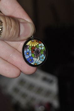 a person is holding a colorful flower glass cabochon in their left hand,