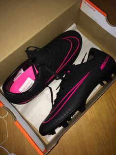 a pair of black and pink soccer shoes in a box on a wooden table with wires