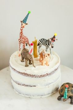 a white cake topped with animals and decorations on top of a marble counter next to a tortoise