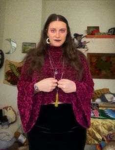 a woman standing in a room wearing a purple sweater and black skirt with her hands on her hips