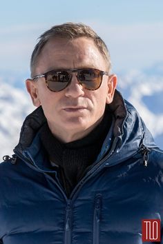 a man with sunglasses on standing in front of snow covered mountains and looking at the camera