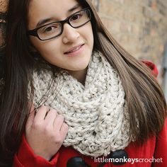 a woman wearing glasses and a knitted cowl is standing in front of a brick wall