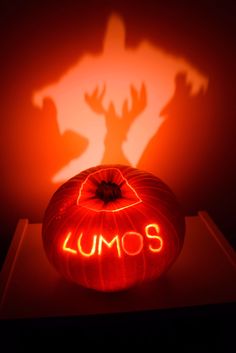 a pumpkin with the word lumos carved into it in front of a shadow of a demon