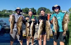 four people holding up some fish on a dock