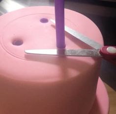 a pink cake with a pair of scissors sticking out of it