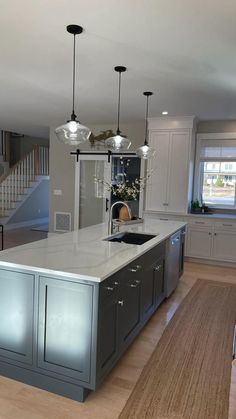 a large kitchen with an island in the middle and two lights hanging from the ceiling