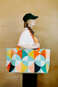 a woman is holding a multicolored tote bag