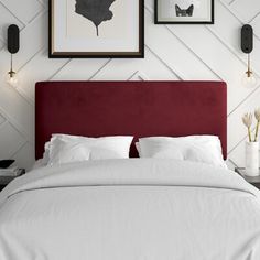 a bed with white sheets and pillows in front of two framed pictures on the wall