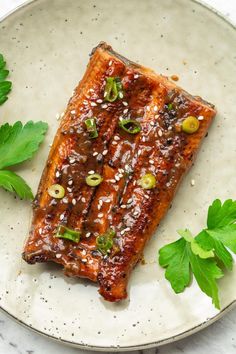 a white plate topped with meat covered in sauce and garnished with green leaves