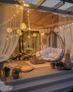 an outdoor area with hanging chairs, lights and curtains on the roof above it is lit up by string lights