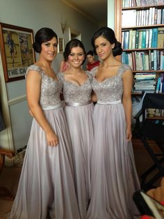 three beautiful women standing next to each other in front of a book shelf filled with books