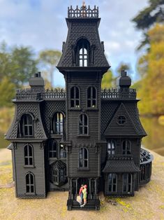 a black doll house with two people standing in the front window and on top of it