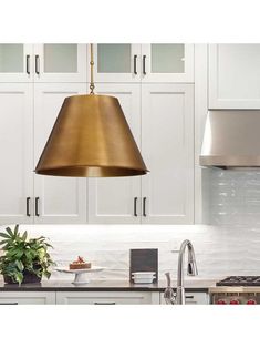 a kitchen with white cabinets and gold pendant light hanging over the stove top, next to a potted plant