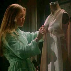 a woman standing next to a dress on a mannequin's dummy wearing a green robe