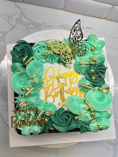 a birthday cake decorated with green frosting and gold decorations on a marble table top