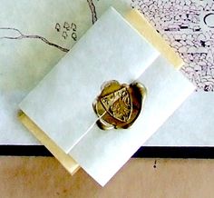 an envelope with a wax stamp on it and a gold ring in the middle, sitting on top of a piece of paper