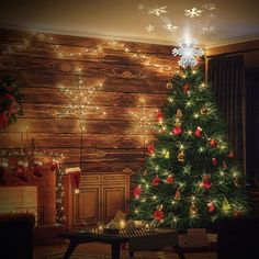 a decorated christmas tree in front of a wooden wall with lights and presents on it