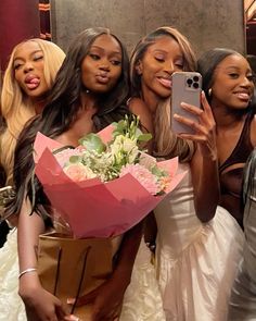 four beautiful women taking a selfie in front of a mirror holding flowers and a cell phone